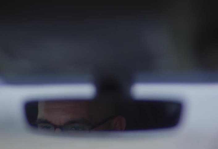 A close up footage of a mirror displaying a man in a car