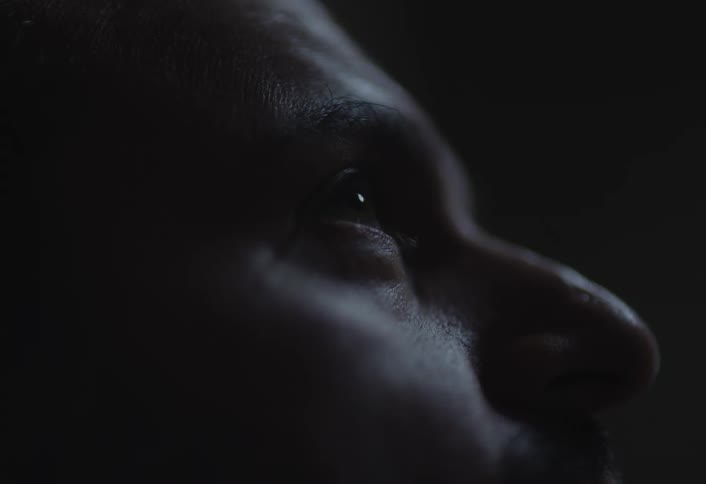 A closeup profile of a mans face gazing upward in a dimly lit environment