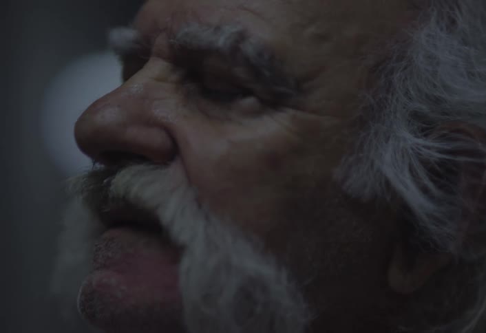 A closeup reveals the weathered face and moustache of a person with white hair
