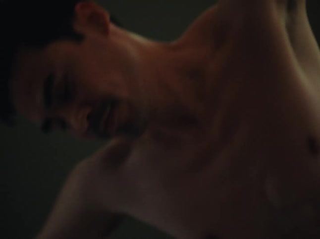 A shirtless male is stretching his arms indoors