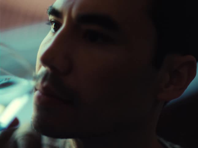 A closeup of a mans face in a dimly lit room as he hesitates to drink from a glass of water showcasing peculiar behavior