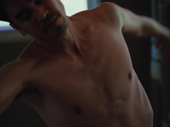 A bare chested man spins gracefully in dance motions within a dimly lit room