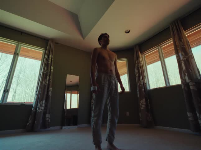 Shirt less male dancer stills to stand in a room with many windows