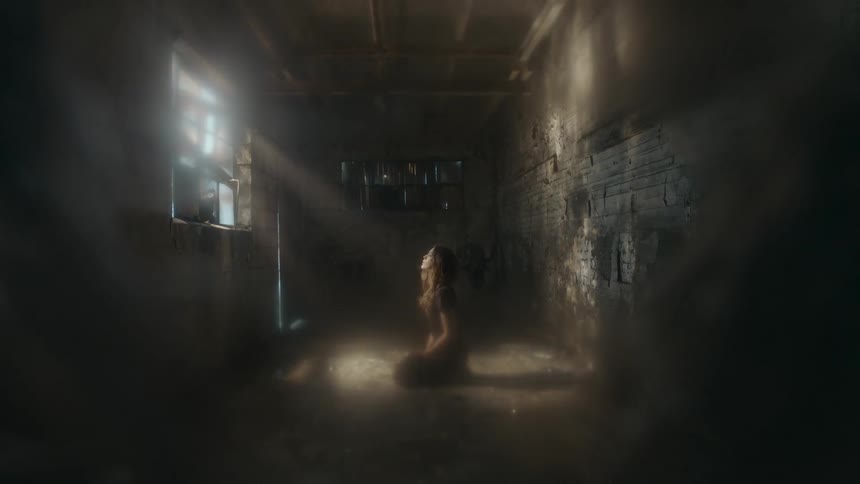 A woman is kneeling in front of a window in a dark room