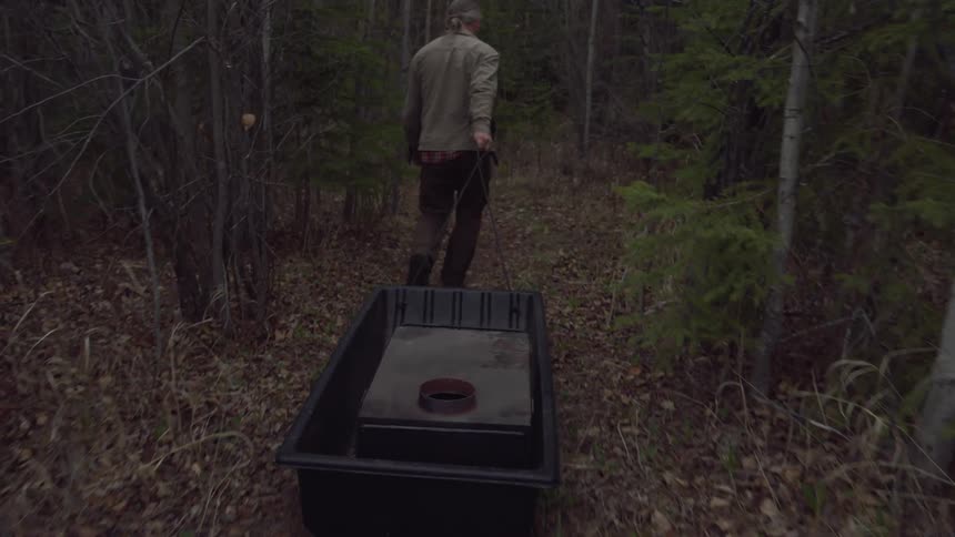 A man drags a small wood stove to his campsite