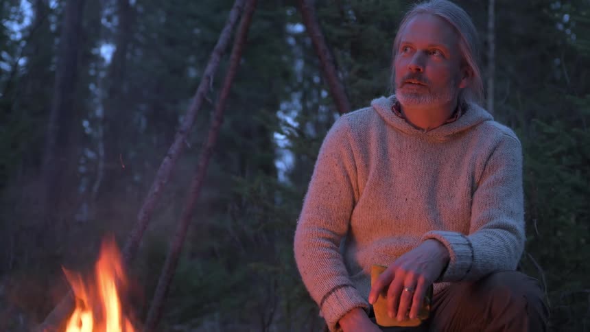 Man sitting near a campfire smiling and chatting