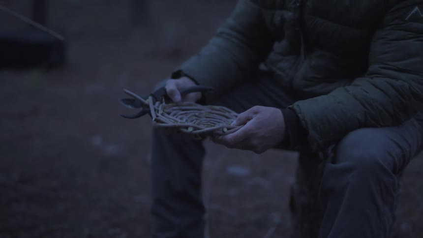 A person is carefully examining and adjusting a woven basket outdoors in dim lighting