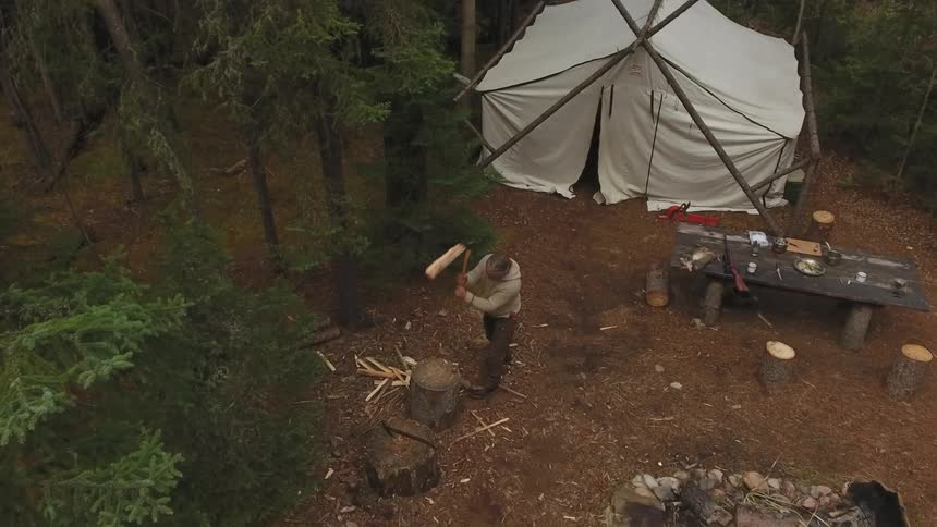 Man cutting wood on a stump in the middle of the forest where he camped
