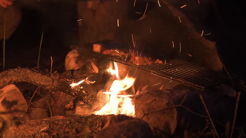Cooking steaks on a grill over a campfire at night