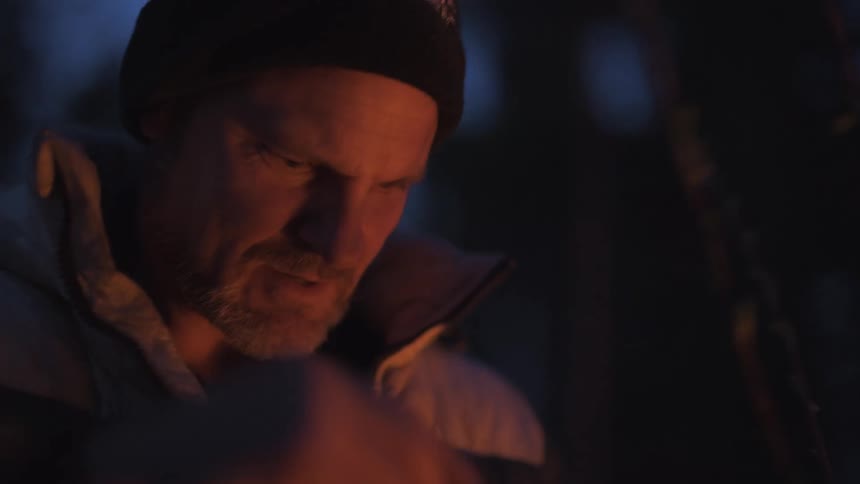 A man outdoors at night gathering branches