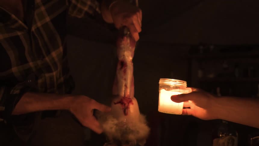 Man skinning a dead rabbit by candlelight outdoors at night