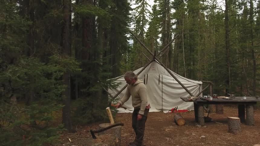 A man camping in a forest chops wood