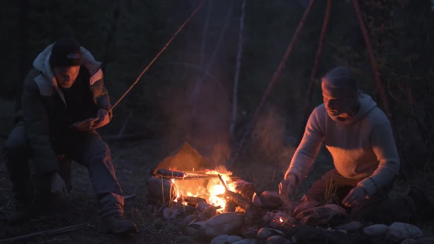 Men talk and cook on the campfire