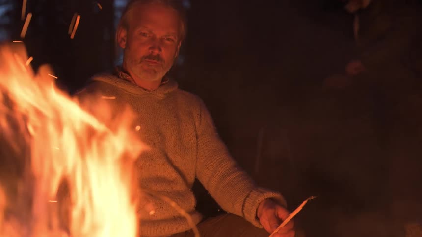 A man watches the campfire at night