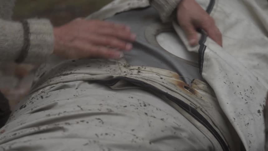 A close up of a mans hands wrapping a large tarp outdoors