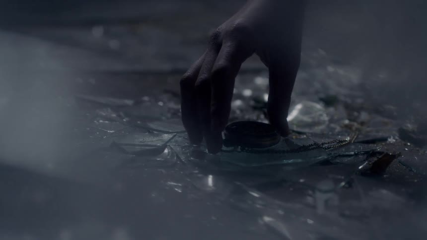 Broken glass is all over the ground, a hand picks up a pocket watch