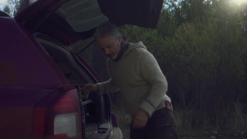 A hunter loads a couple of rabbits onto the back of a car on a rural road in the morning