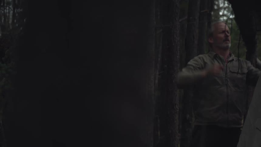 A man is setting up his tent in the woods