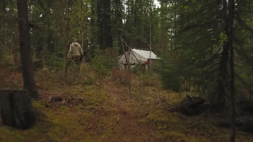 Hunter carrying two dead animals in one hand as he walks through the forest towards his cabin
