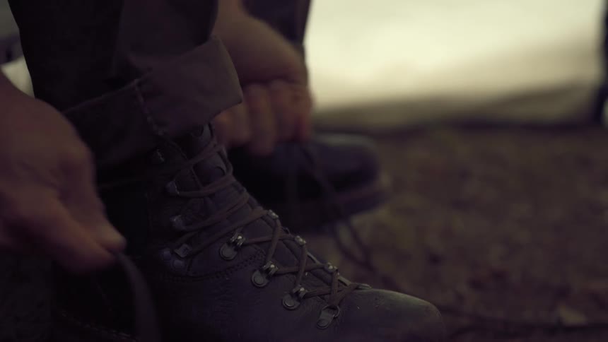 A mans hands tying the laces of a dark worn boot