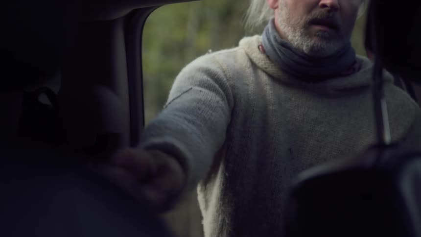 Man walking back from the forest putting a rifle in back seat of car