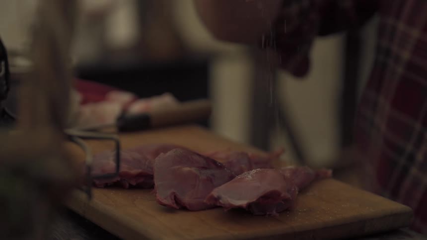 A man sprinkles salt on pieces of meat