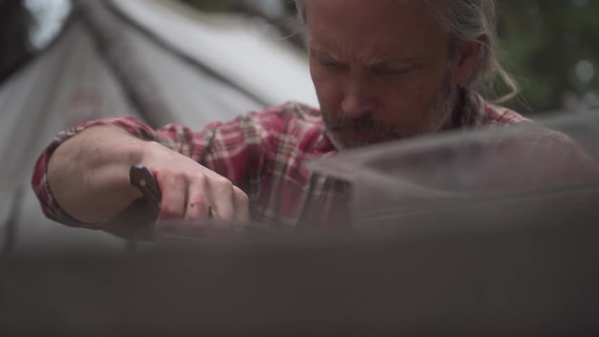 A man is skinning a rabbit at his camp