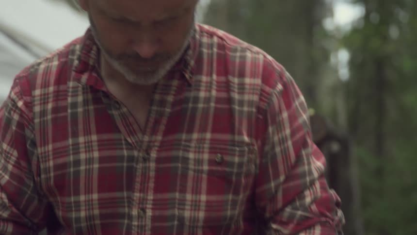 A hunter skins a game rabbit with his hands on a wooden table outdoors