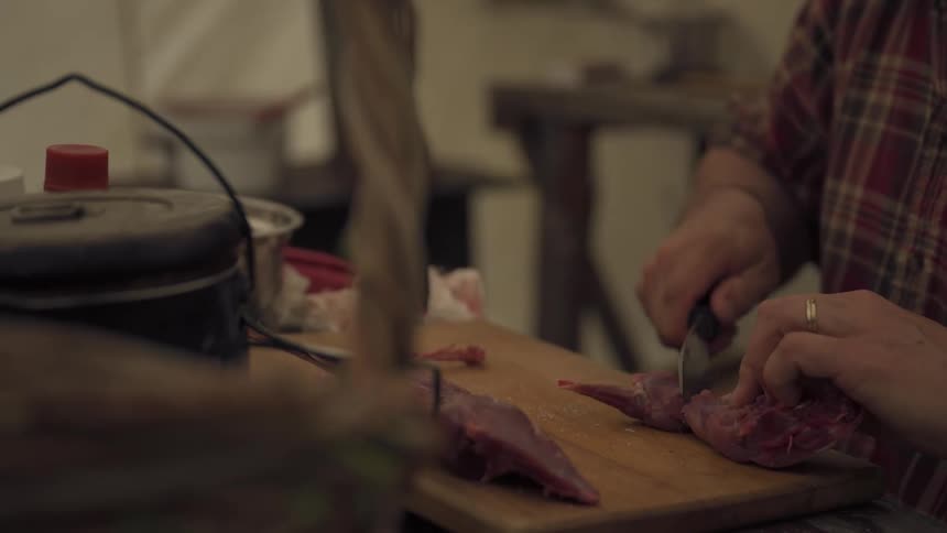 Man separates pieces of an animal carcass while sitting at a table in a camp