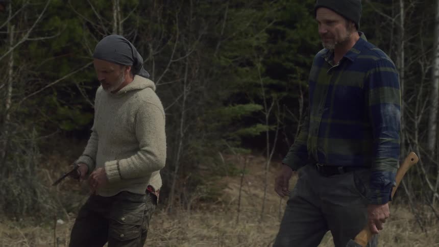 A man hands another man an axe to cut a log