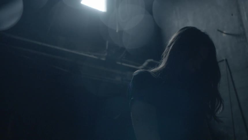 A woman looks up at a single window in a dark room