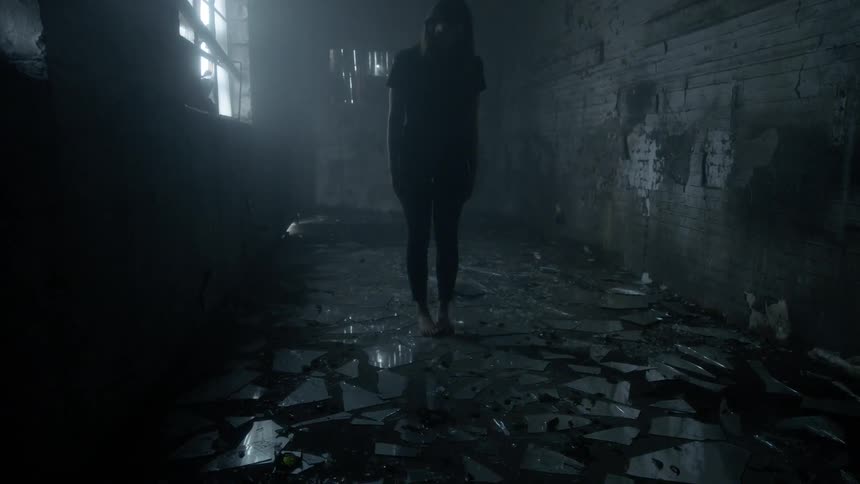 A woman is standing in a dark room with glass all over the ground