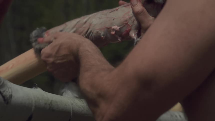 A man hangs animal skin on the log