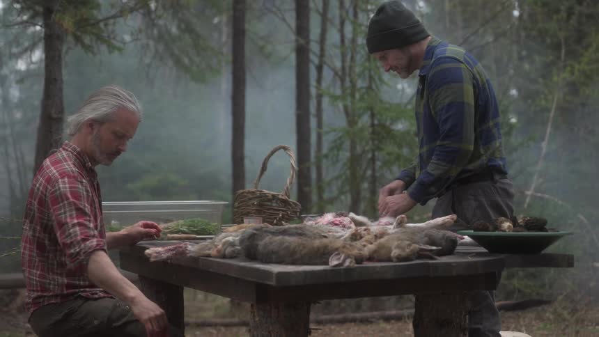 Hunters clean the game they have killed while at a table near the foggy woods