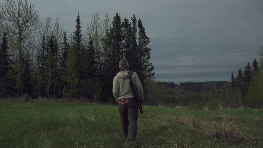 A hunter with a rifle over his shoulder walking towards a tree line