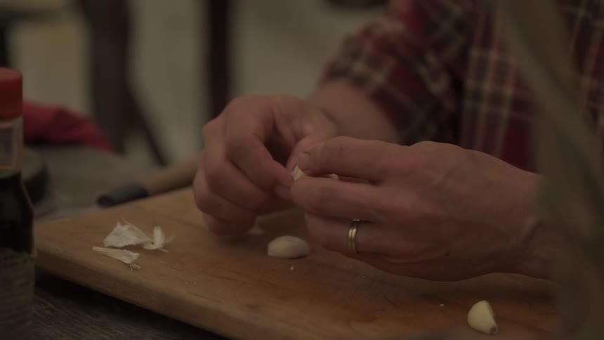 A man peeling garlic gloves on a wooden cutting board