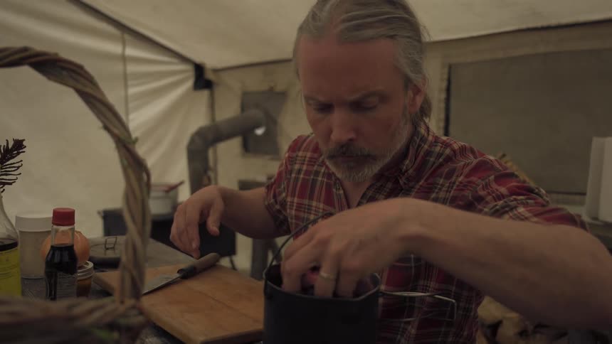 A man puts meat and bones in the pot inside his tent