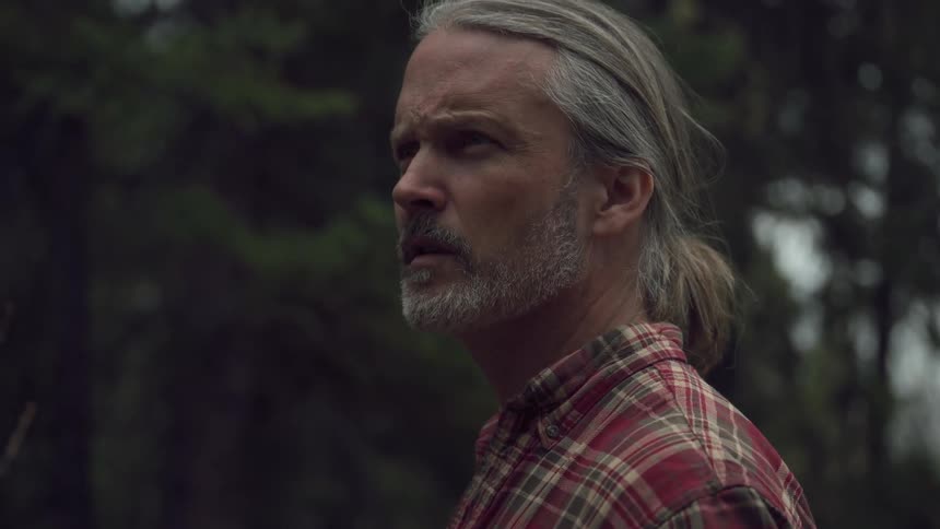 Older man standing in the woods looks around