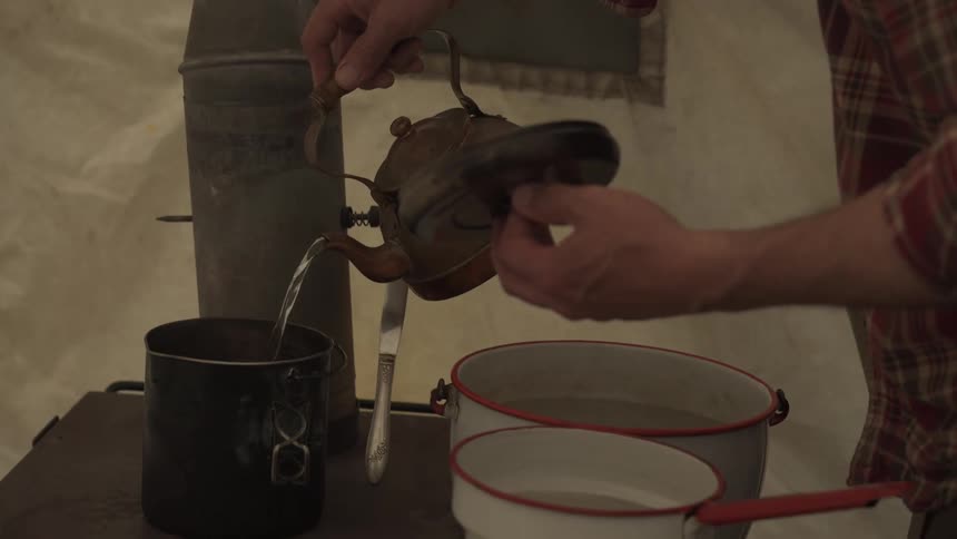Person taking a kettle from the stove and pouring water into another pot