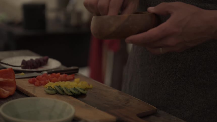 Placing sliced kiwis from a wood bowl next to cut produce on a cutting board