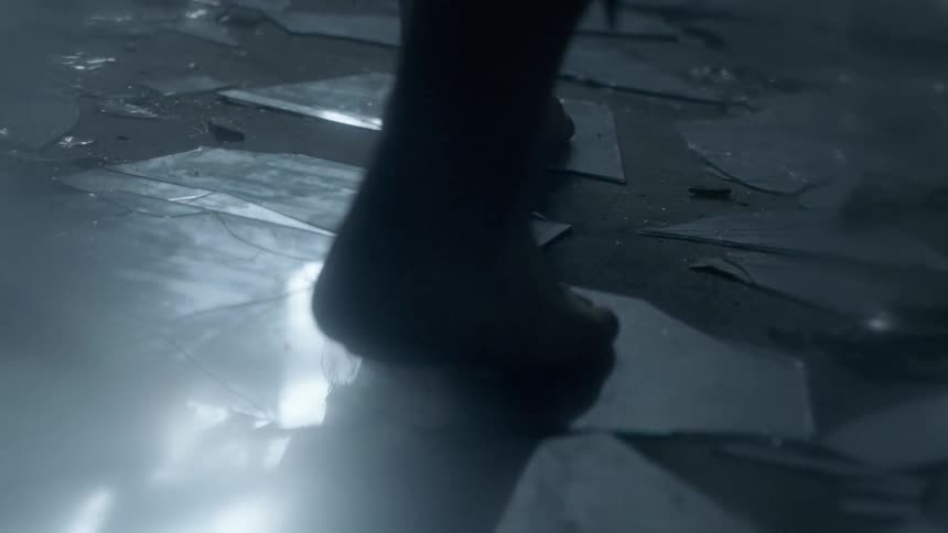 A person walks over broken glass in a dark room