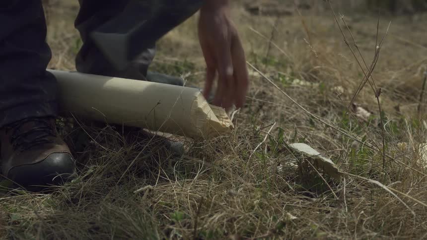 A close up of a person using an axe to shape the tip of a log in a grassy field