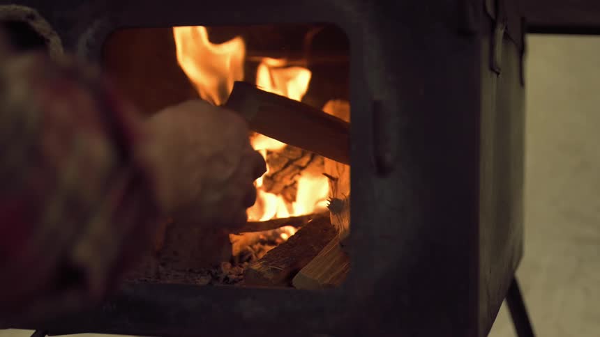 A man is feeding wood into a fire into a wood stove