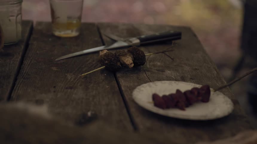 A man is making dinner and puts a skewer of mushrooms on a plate