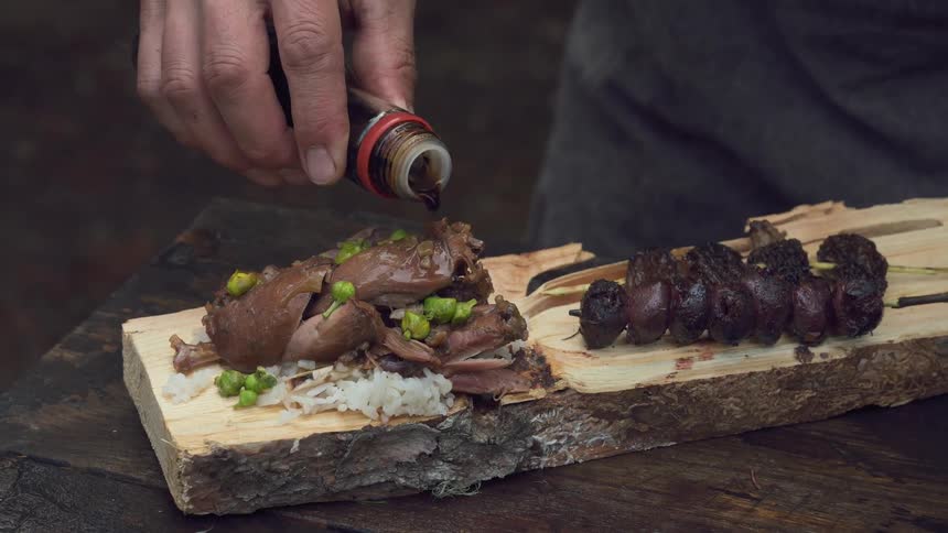 A persons hand putting sauce on top of food on a wooden board