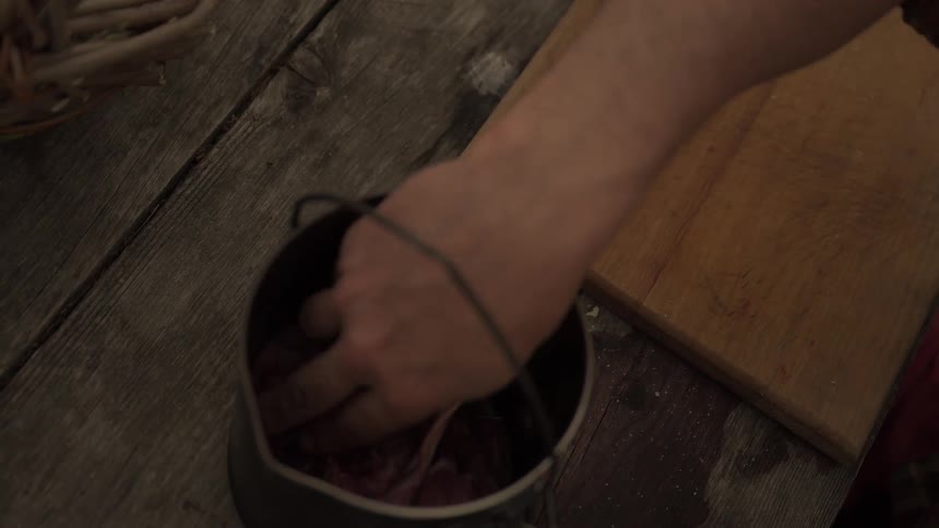 A person places pieces of raw meat likely rabbit or poultry into a metal pot on a wooden table