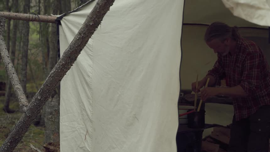 A man is stirring a pot in his tent