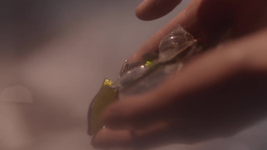 Shards of glass fall out of a woman's hands