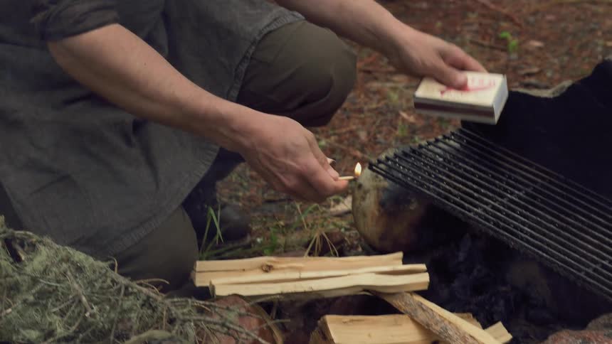 A man lights a piece of tinder with a match