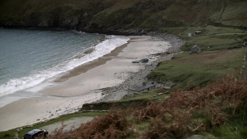Waves coming ashore on a beach area as a vehicle approaches and stops in a parking area